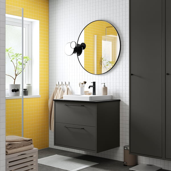 Dark grey HAVBÄCK vanity with drawers, white basin, large mirror, yellow & white tiles, window with plant.