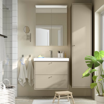Minimalist bathroom with beige HAVBÄCK vanity, modern sink, large mirror, hanging towels, and plants.