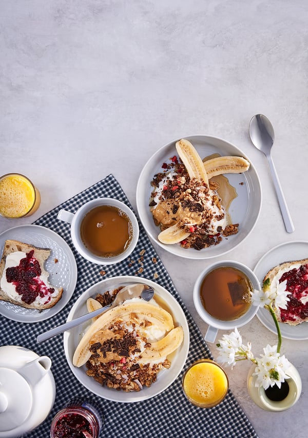 Breakfast spread with HJÄLTEROLL muesli bowls, toast, coffee, orange juice, flowers.