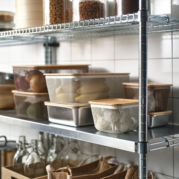Metal shelving unit organising kitchen items, featuring stacked mesh baskets with wooden lids, storing fruits and bottles efficiently.