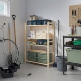 A garage with wooden IVAR shelves holding tools and items. The large light-colored shelf stands tall with green bins and other stored items.