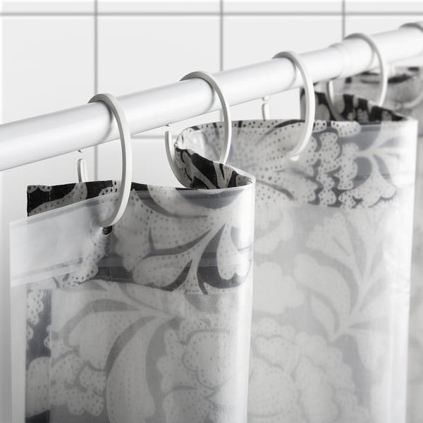 This image shows a white shower curtain rod with multiple metal rings holding a black and white floral shower curtain.