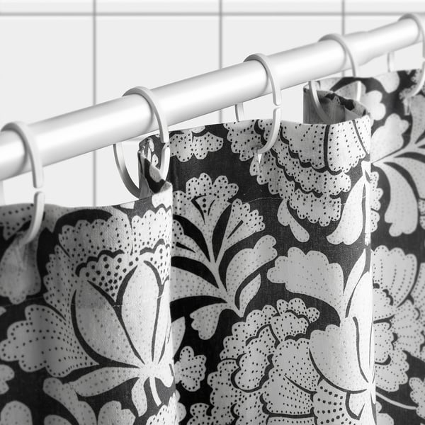 Black-and-white floral shower curtain hangs from rods with hooks, creating a decorative bathroom divider.