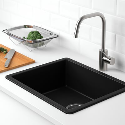 Black kitchen sink with stainless steel tap, featuring a colander with broccoli and cutting board with knife nearby.