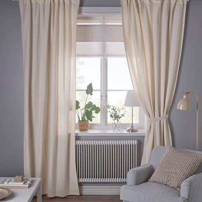 Off-white curtains hang from a tall window against a dark grey wall. A striped chair and floor lamp are below.