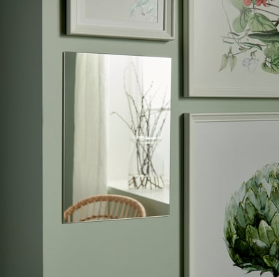 Small, rectangular silver-framed mirror hangs on green wall, bordered by framed nature prints.