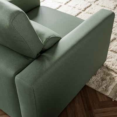 Green upholstered armchair with clean lines and supportive cushions, placed on a white shaggy rug and hardwood floor.