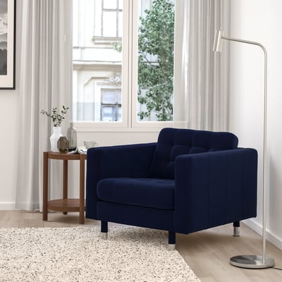 Modern living room: navy blue MORABO armchair, chrome legs, soft velvet, cosy and stylish next to large window.