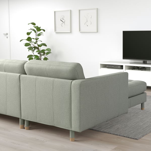 Modern light green sectional sofa with wooden legs and cushioned seats against a white wall, styled with tv and decorations for a cosy look.