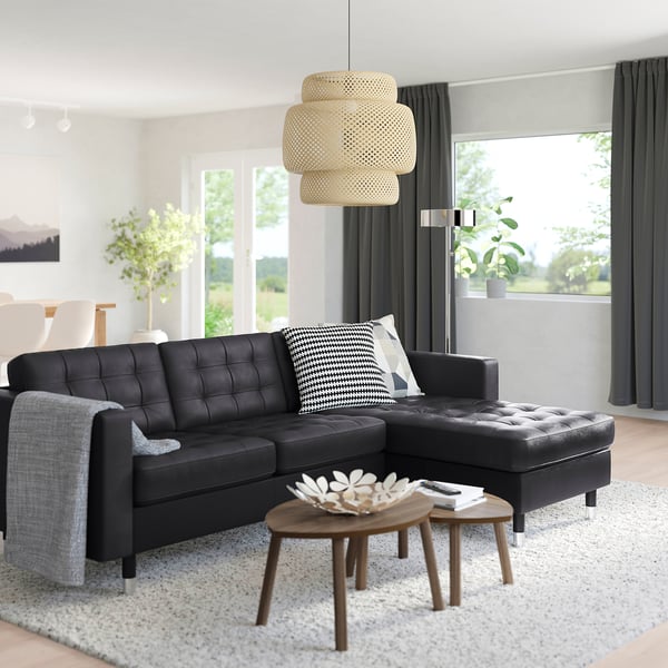 Modern living room with black l-sofa, pendant light, coffee tables, & large windows.