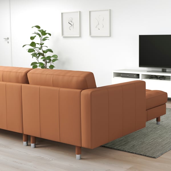 Modern living room with orange sofa, tv, plant, and white walls.