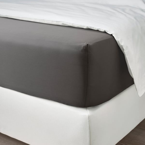 A neatly made bed with dark grey sheets and a white pillowcase, showcasing soft fabric and decorative fold.