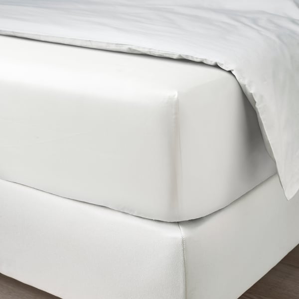 A neatly made bed with crisp white sheets, featuring a smooth, double-layered top edge. The fitted sheet hugs the mattress corners perfectly.