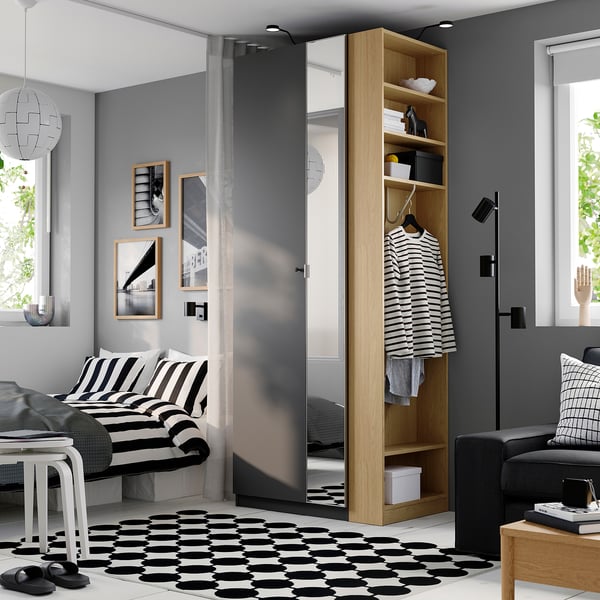Modern bedroom with tall, light PAX wardrobe and mirror, beside striped bed, on patterned rug, with books and art.