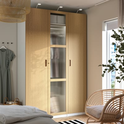 PAX wardrobe in natural oak with frosted glass and mesh baskets beside bed and window.