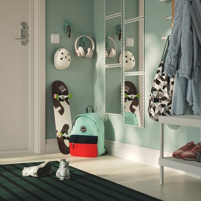 Hallway with green wall and grouped wavy RUNDOXEL mirrors reflecting items like skateboard, helmet, headphones, and mint green backpack.