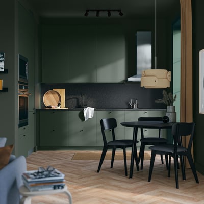 Modern kitchen with SEKTION dark green cabinets, black chairs, wooden floor, track lighting, and a yellow accent piece.