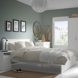 Modern bedroom with SONGESAND bed, white linens, slippers, books, photos, mirror.