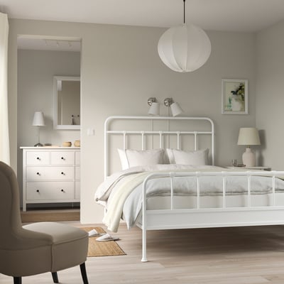 Minimalist bedroom with white STJÄRNÖ bed, pendant light, dresser, mirror, beige armchair, jute rug.