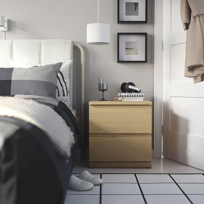 Minimalist bedroom with STORKLINTA wooden bedside table. Lamp, books, headphones. Grey bed linens.