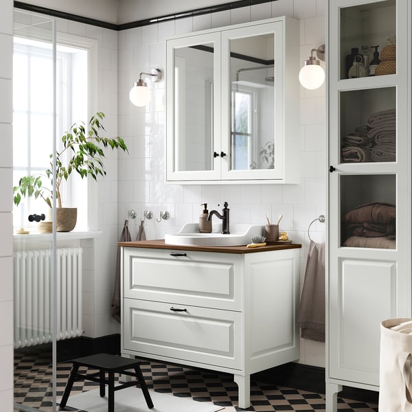 Elegant white TÄNNFORSEN vanity, rectangular sink, wall-mounted cabinets, black floor tiles, radiator, plant.