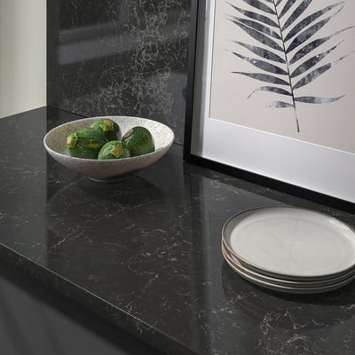 Black marble countertop with bowl of green tomatoes and stack of white plates, framed leaf art on wall.