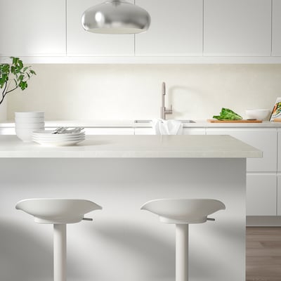 Modern minimalist kitchen with TÄRNHULT white glass wall panels, sleek countertops, chrome tap, green plants, and white bar stools.