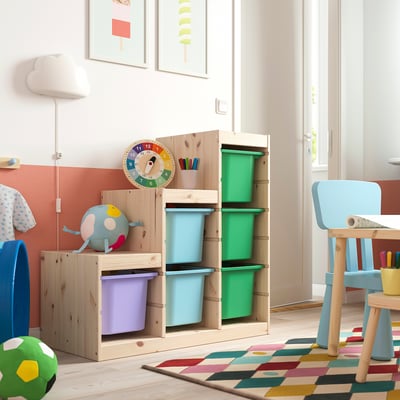 Kids play area with TROFAST storage, colourful boxes, clock, toy, chair, and rug.