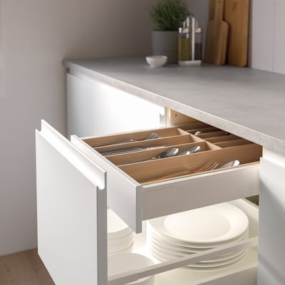 Open kitchen drawer revealing organised cutlery tray with compartments, plates below.