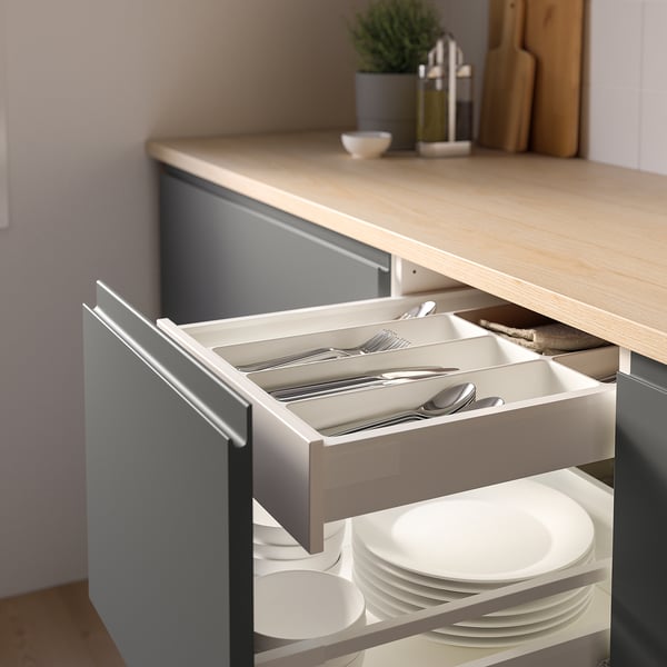 Open kitchen drawer with cutlery organiser, holding forks, knives, spoons, and plates.