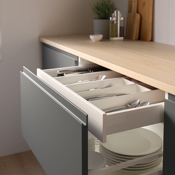 Kitchen drawer with organised cutlery: forks, knives, spoons. Light counter, plants.