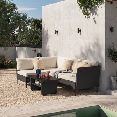Backyard lounge set with beige cushions, black wicker, & concrete wall.