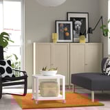 Modern living room with orange rug, white table, grey sofa, black-white chair, wood cabinet, & framed pictures.