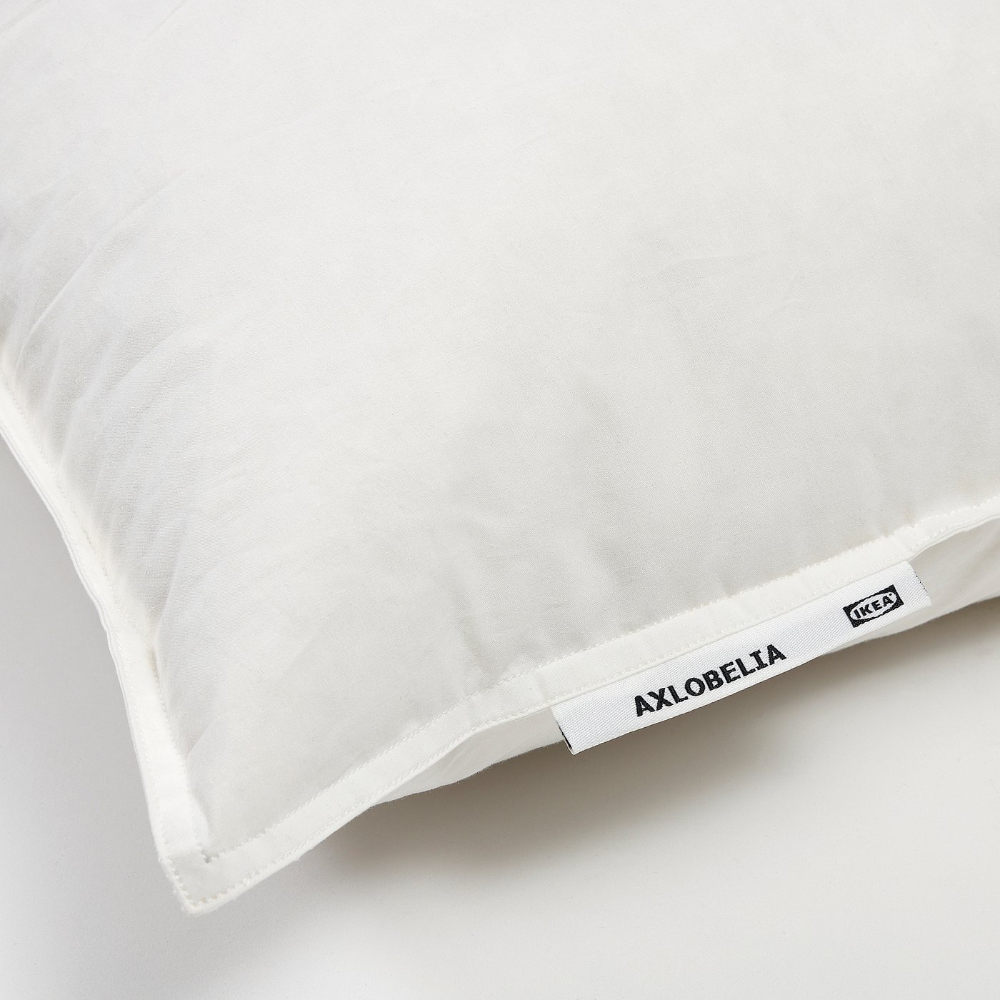 Close-up of a soft, white pillow with AXLOBELIA brand tag, high-quality cotton and feather filling, ideal for side or back sleepers.