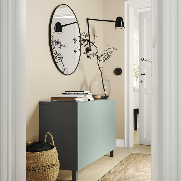 Modern entryway with light blue BESTÅ storage unit, black accents, round mirror, wall lamps, and a large woven basket.