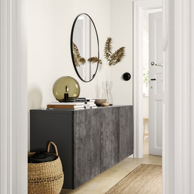 Modern entryway with BESTÅ grey storage unit, round mirror, lamp, flowers, basket, and white doors.