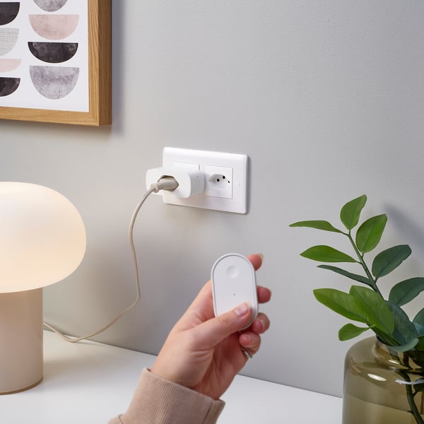 Hand holding remote control adjusting smart plug connected to lamp.