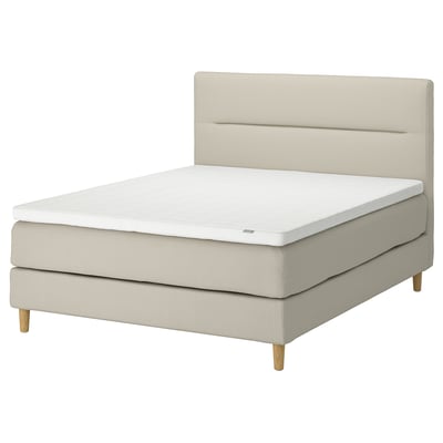 A beige upholstered HEMFJÄLLET divan bed with a soft headboard, wooden legs, and a white mattress.