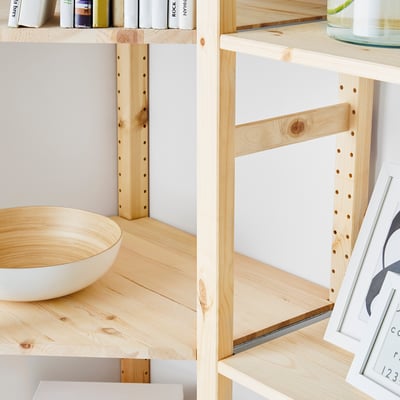 Wooden IVAR shelving unit with adjustable shelves displaying various items including books, bowl, and framed art.