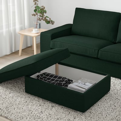 Green KIVIK footstool with storage open, showing magazines, on white rug near window.