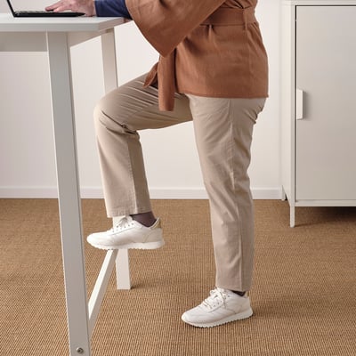 Person leaning on high table with footrest, using laptop.
