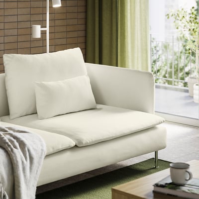 Modern white sofa with light green curtains, balcony view, coffee mug on table.