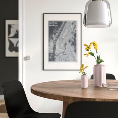 Minimalist dining area with wooden table, pink vases, map poster, and black chairs.
