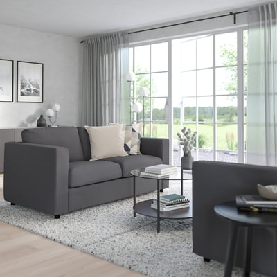 Modern living room: VIMLE grey sofa, 3 cushions, end table, tall floor lamp, large window with view.