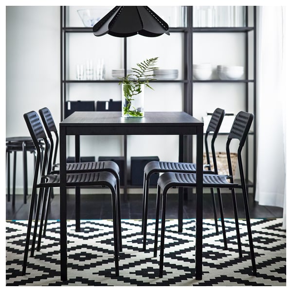 Moderní černý jídelní set se čtvercovým stolem, čtyřmi stohovatelnými židlemi a geometrickým kobercem; Minimalistický design.