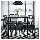 Moderní černý jídelní set se čtvercovým stolem, čtyřmi stohovatelnými židlemi a geometrickým kobercem; Minimalistický design.