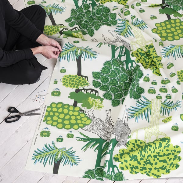 Osoba stříhající zelenou látku s lesní tématikou, pravděpodobně pro šicí projekty.
