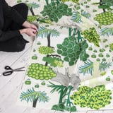 Osoba stříhající zelenou látku s lesní tématikou, pravděpodobně pro šicí projekty.