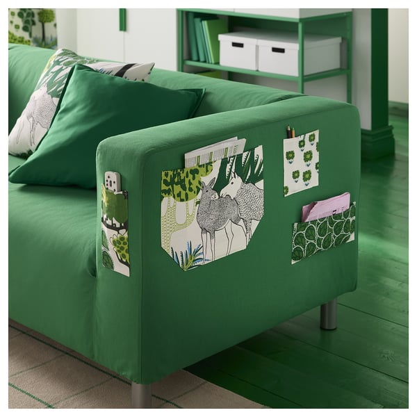 Jasně zelená pohovka s květinovými vzory, s úložnými kapsami a polštáři, umístěná na sladěné zelené polici.