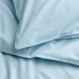 Měkká, světle modrá souprava povlečení vyrobená ze 100% předeprané bavlny, úhledně složená s hladkou strukturou a jemným prošíváním.